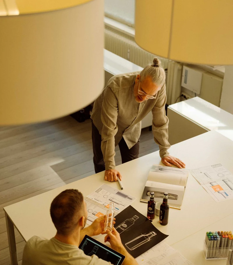 Due persone discutono progetti di design farmaceutico su un tavolo con schizzi e bottiglie.