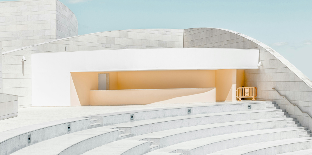 Struttura moderna in cemento e curve geometriche, cielo azzurro; design architettonico pulito e minimalista.