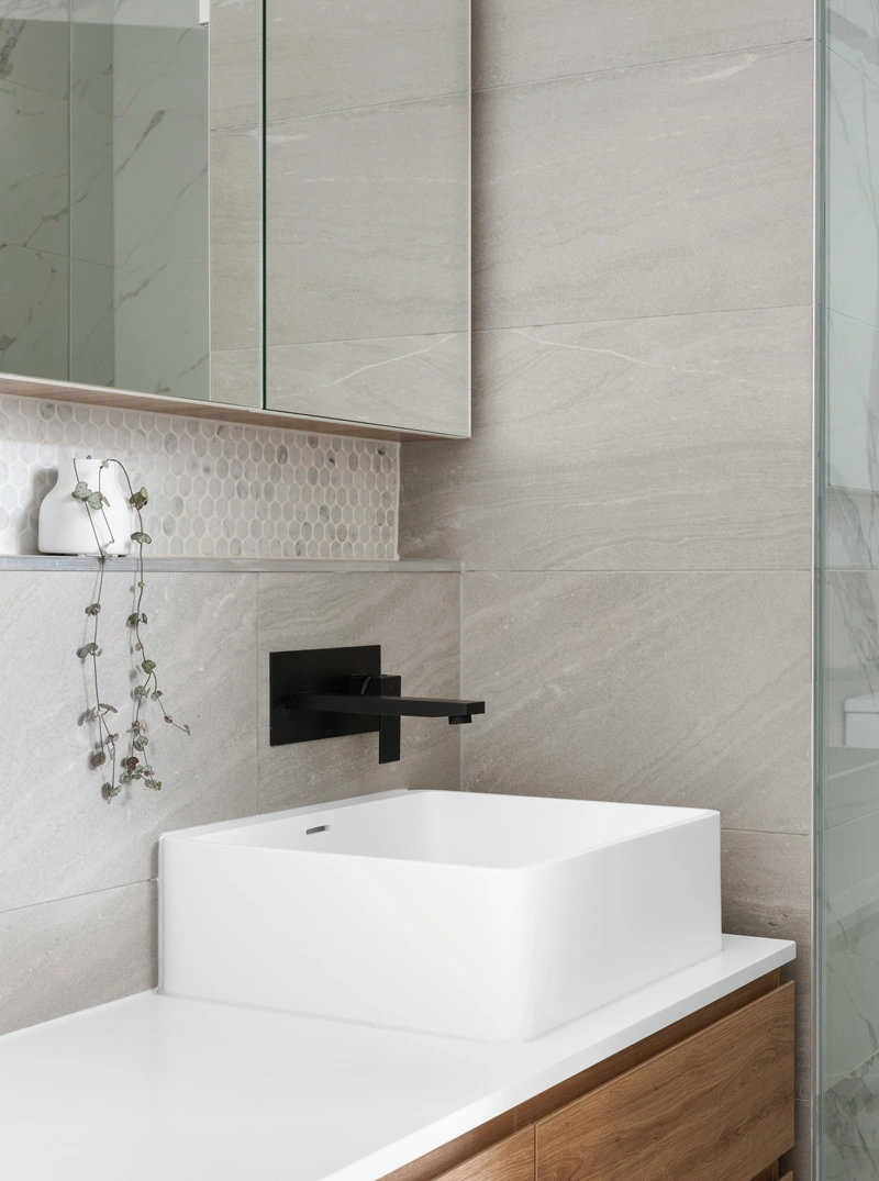 Bagno minimalista con mobile in legno, lavabo bianco e rubinetto nero su sfondo di piastrelle moderne.