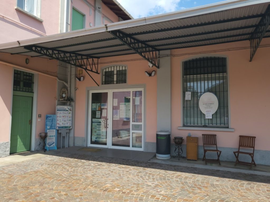 Ingresso di una struttura sanitaria con segnaletica e sedie all'esterno, cielo sereno sopra l'edificio.