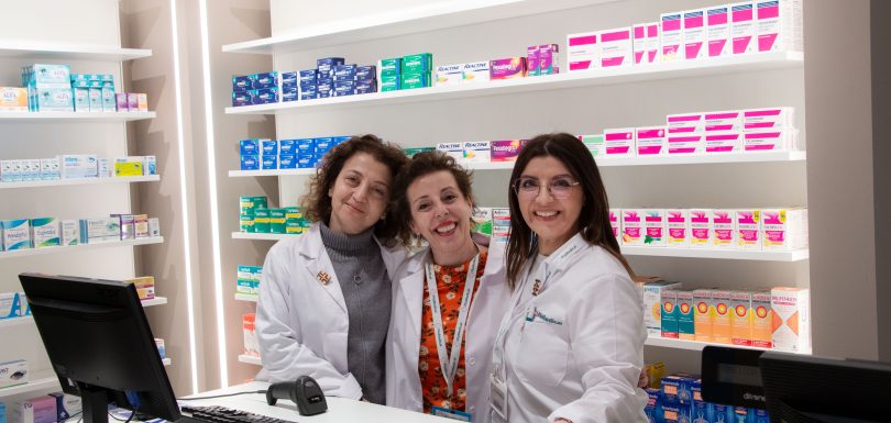 Pharmacy staff smiling behind the counter with a variety of medication displayed on shelves.