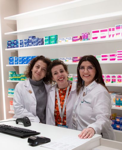 Pharmacy staff smiling behind the counter with a variety of medication displayed on shelves.