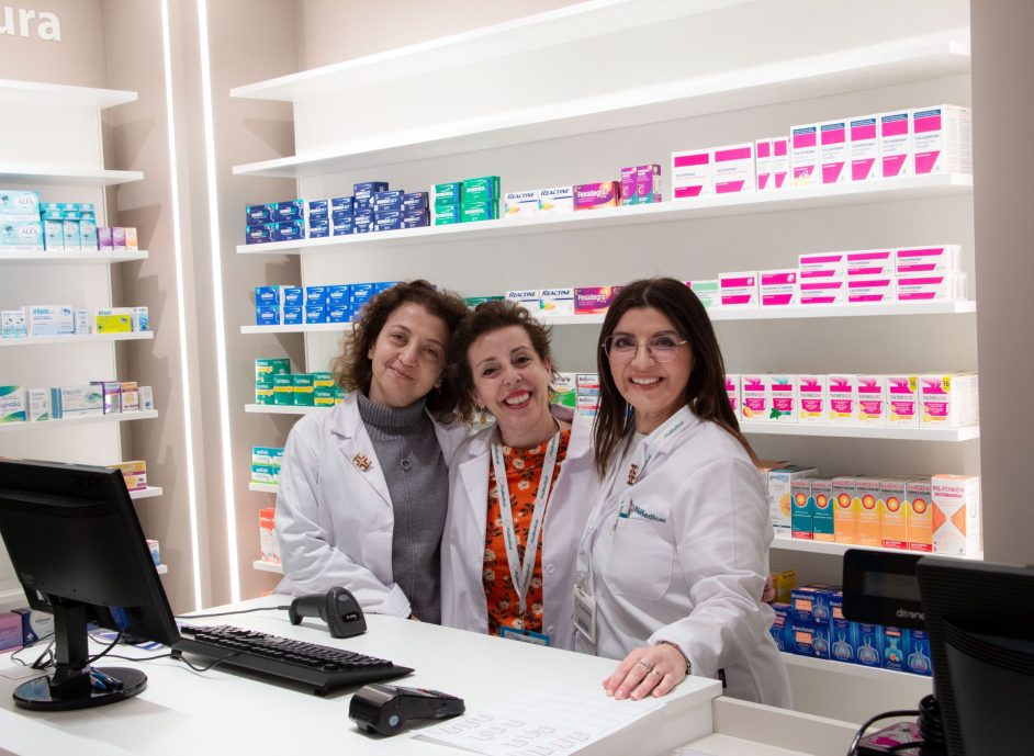 Pharmacy staff smiling behind the counter with a variety of medication displayed on shelves.