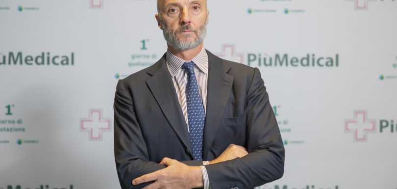 A professional in formal attire standing confidently at a pharmaceutical event backdrop with branding.