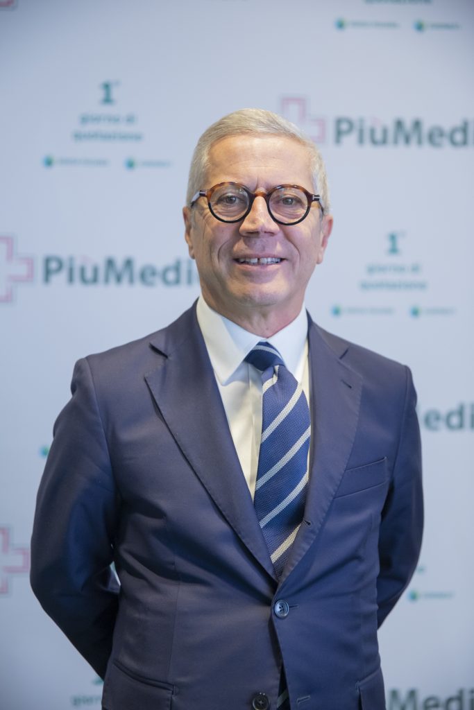 Persona in abito elegante durante un evento di settore farmaceutico con sfondo di brand PiuMedi.