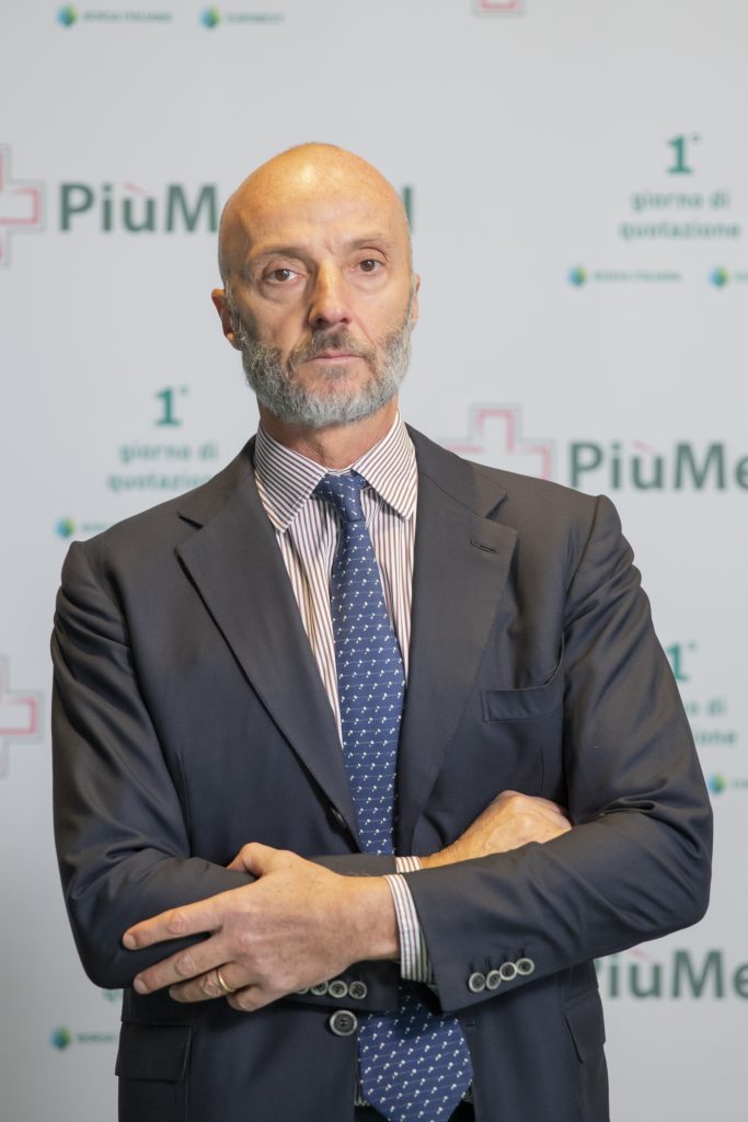 Uomo in giacca e cravatta a un evento aziendale, sfondo con logo PiùMed.