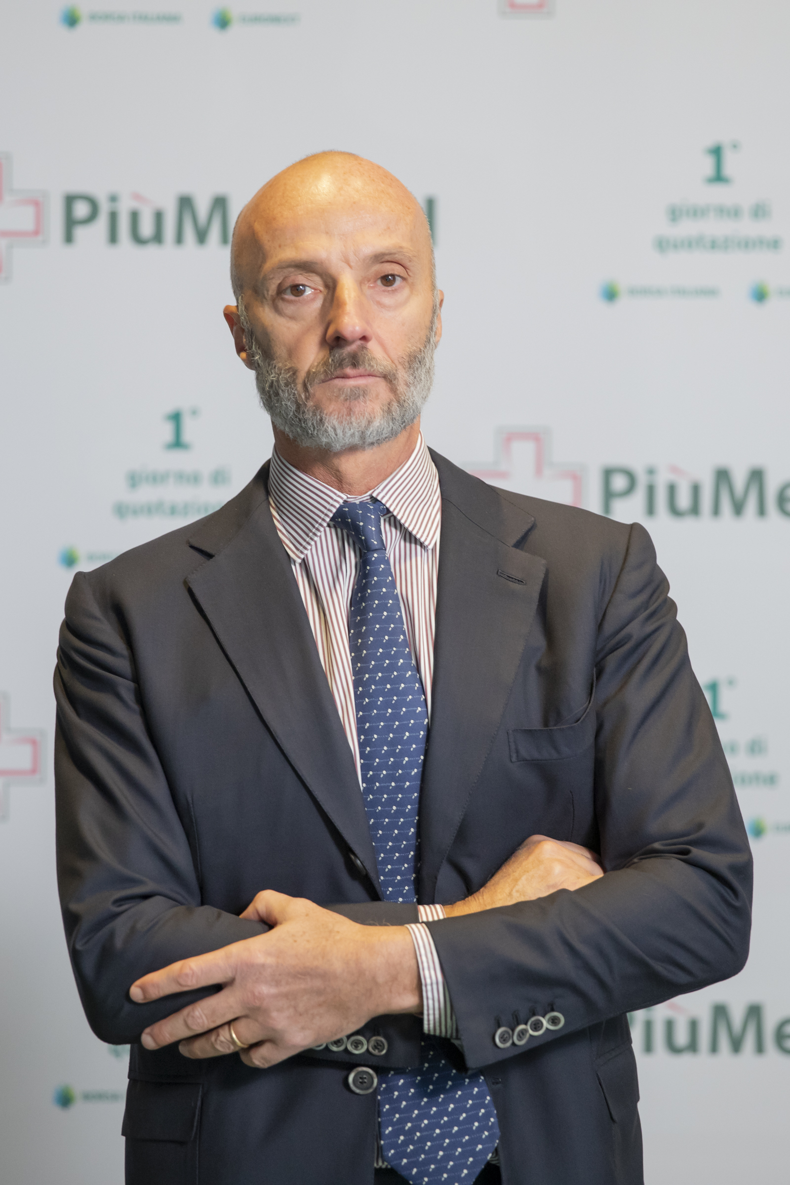 Uomo in giacca e cravatta a un evento aziendale, sfondo con logo PiùMed.